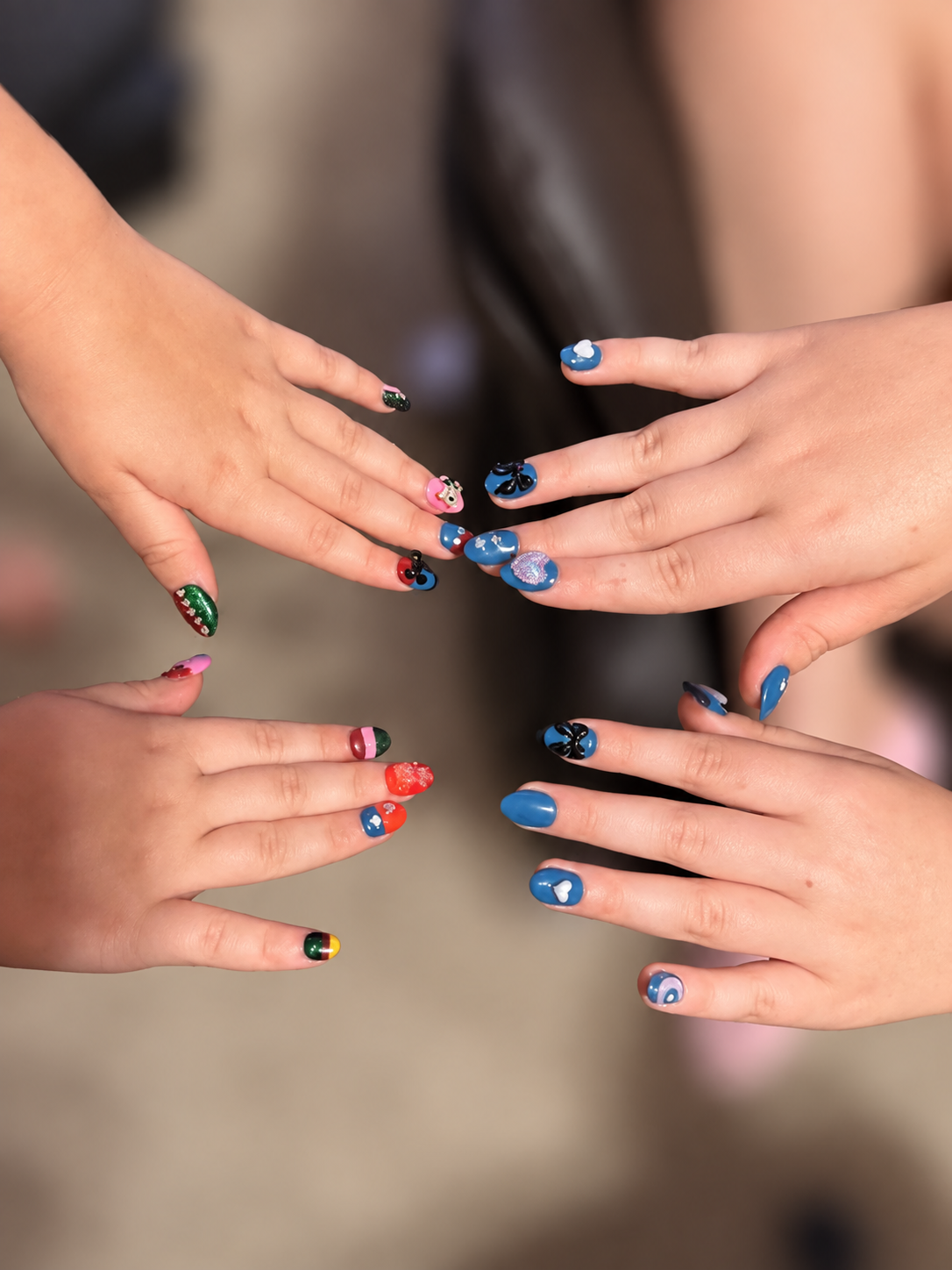 Colorful handmade nail art modeled on hands, with the background blurred